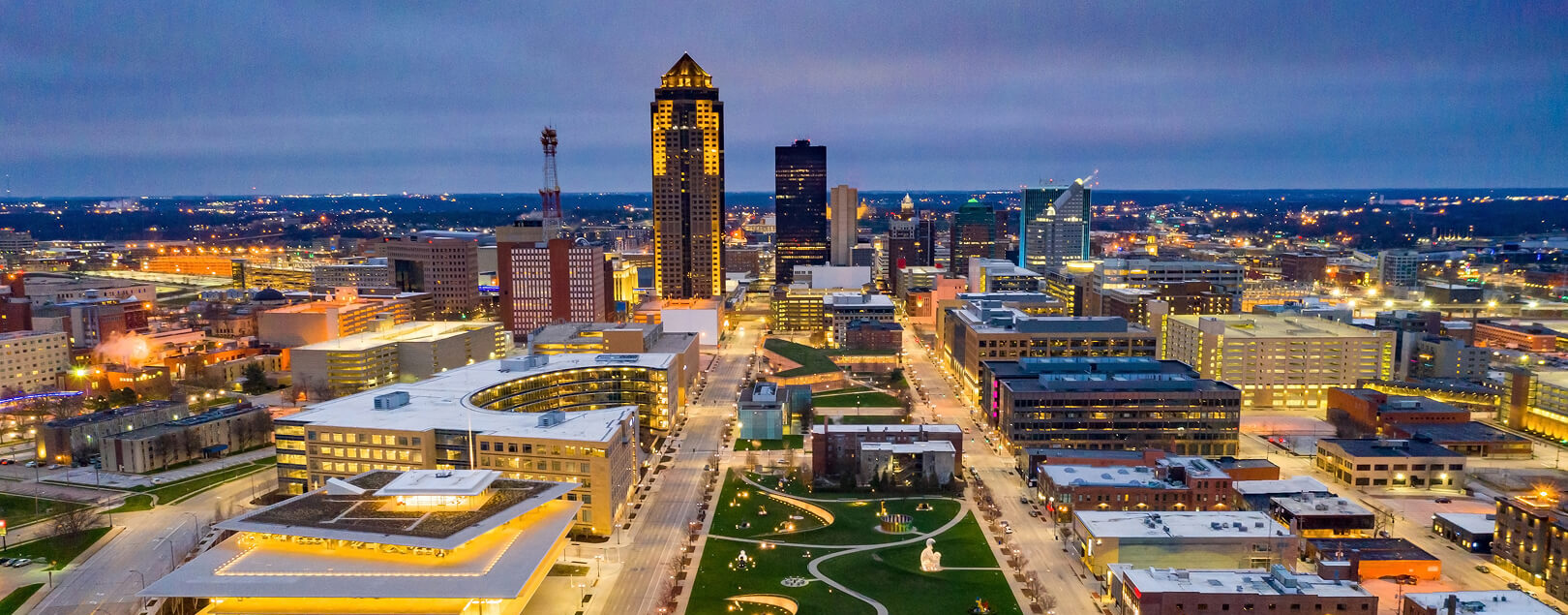 A city scape with a centrally located green space is lit up against a dusky sky