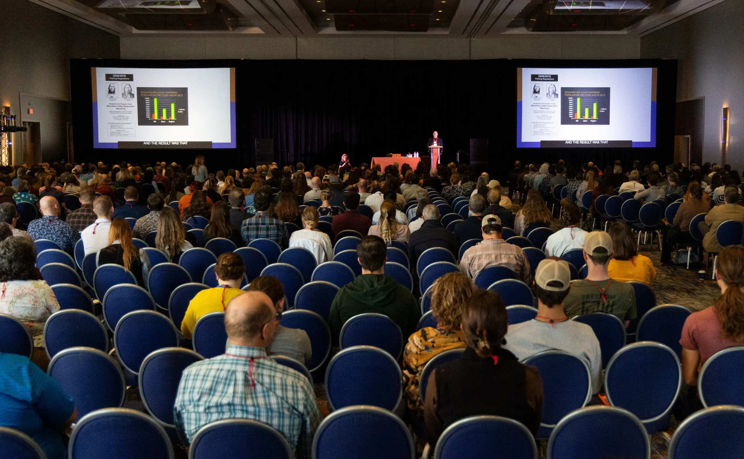 Large audience of zoology students seated in a conference hall attending a session on ecology with a speaker presenting on stage.
