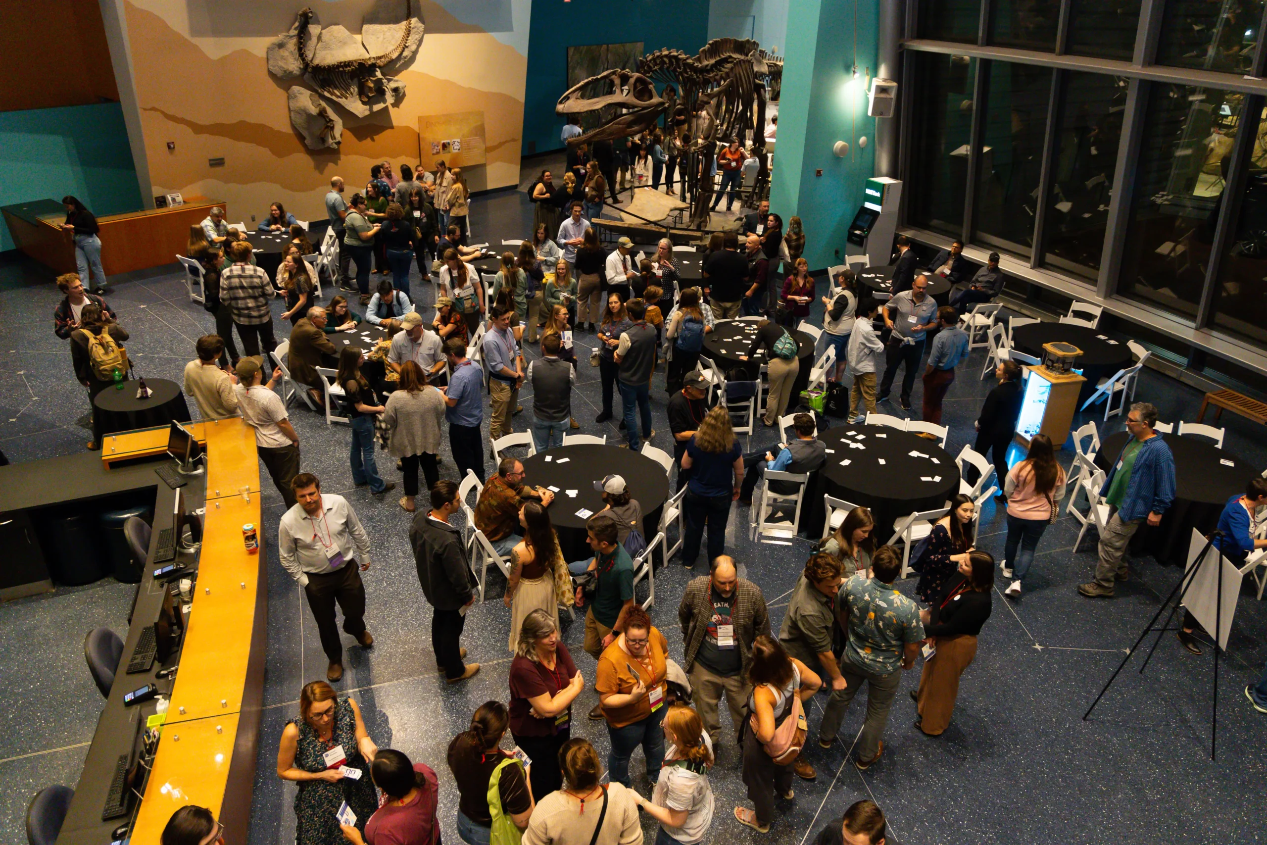Wildlife professionals networking at a conference reception inside a natural history museum with exhibit displays and round tables.