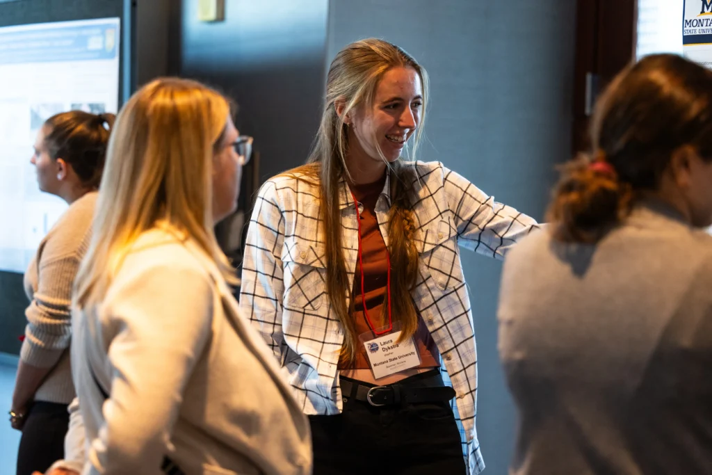 Conference attendees networking and discussing posters during a wildlife science conference, with participants wearing name badges in an indoor event space.