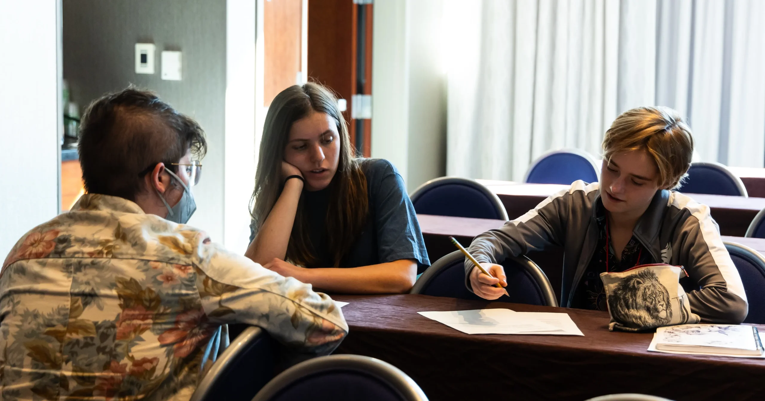 Three conference attendees sit at a table reviewing documents together, representing collaborative discussion on current events and conservation issues.