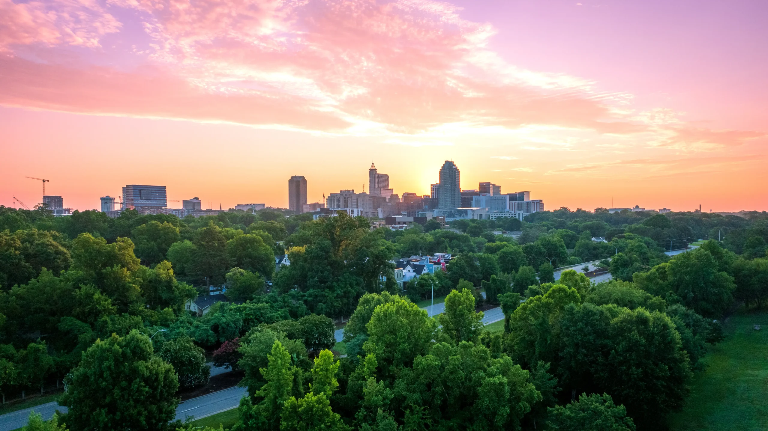City skyline at sunset surrounded by green urban neighborhoods, representing economic growth, sustainable development, and urban expansion.