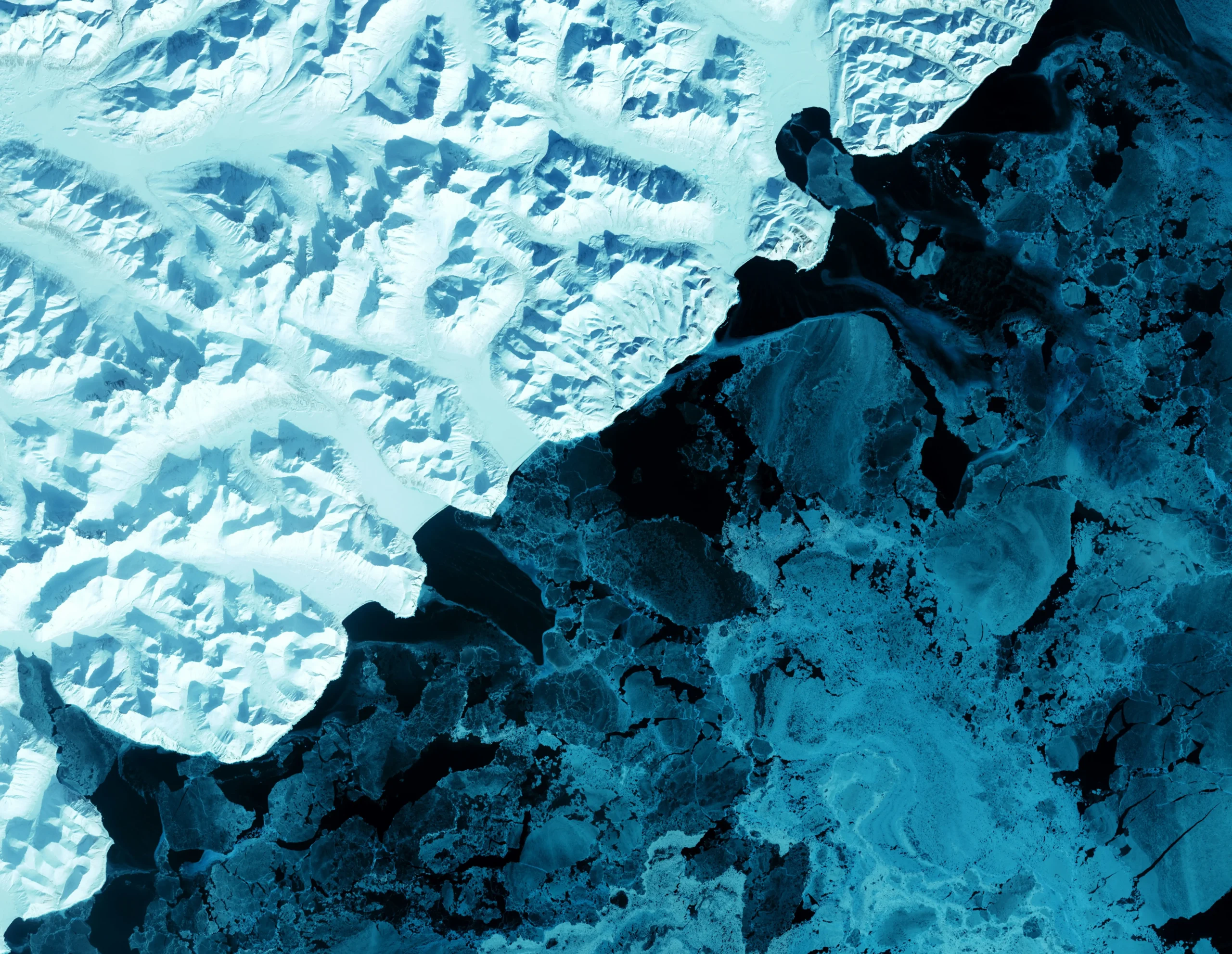 Aerial view of melting glacier ice meeting dark ocean water, showing sea ice breakup and the visible impacts of climate change.