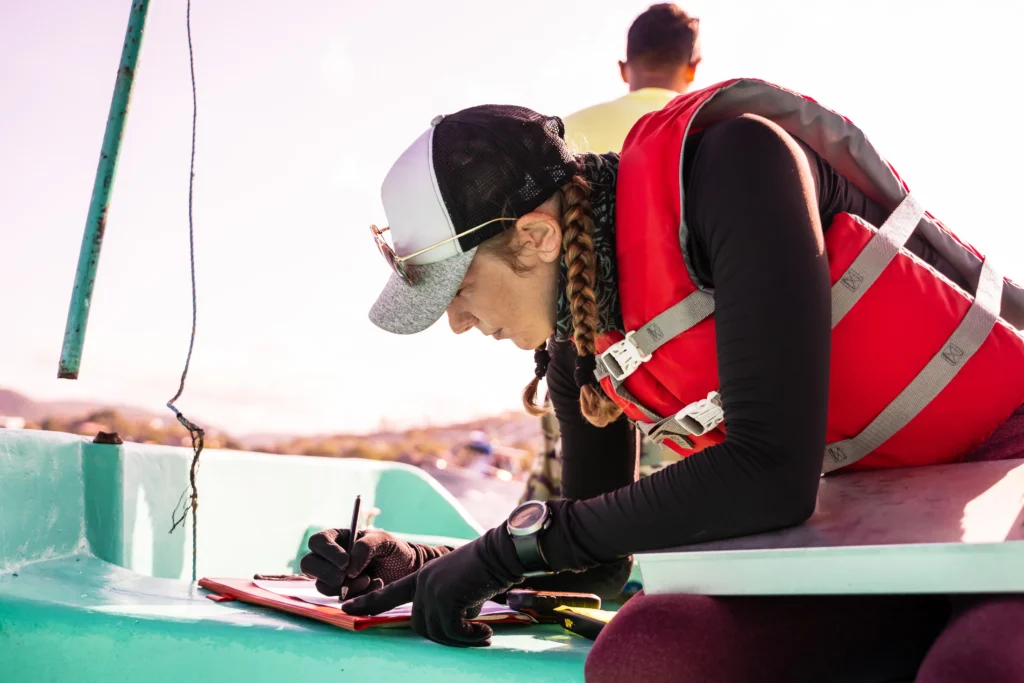 Marine biologist wearing a life jacket recording scientific field data on a research boat during an ocean study, supporting marine conservation and environmental research.