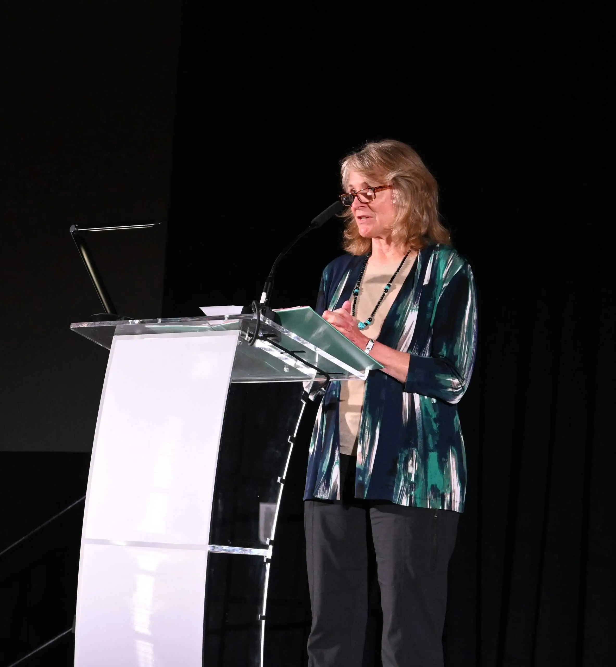 Carol Chambers speaking at a podium during a professional conference presentation, delivering a talk on stage with a microphone and lectern.