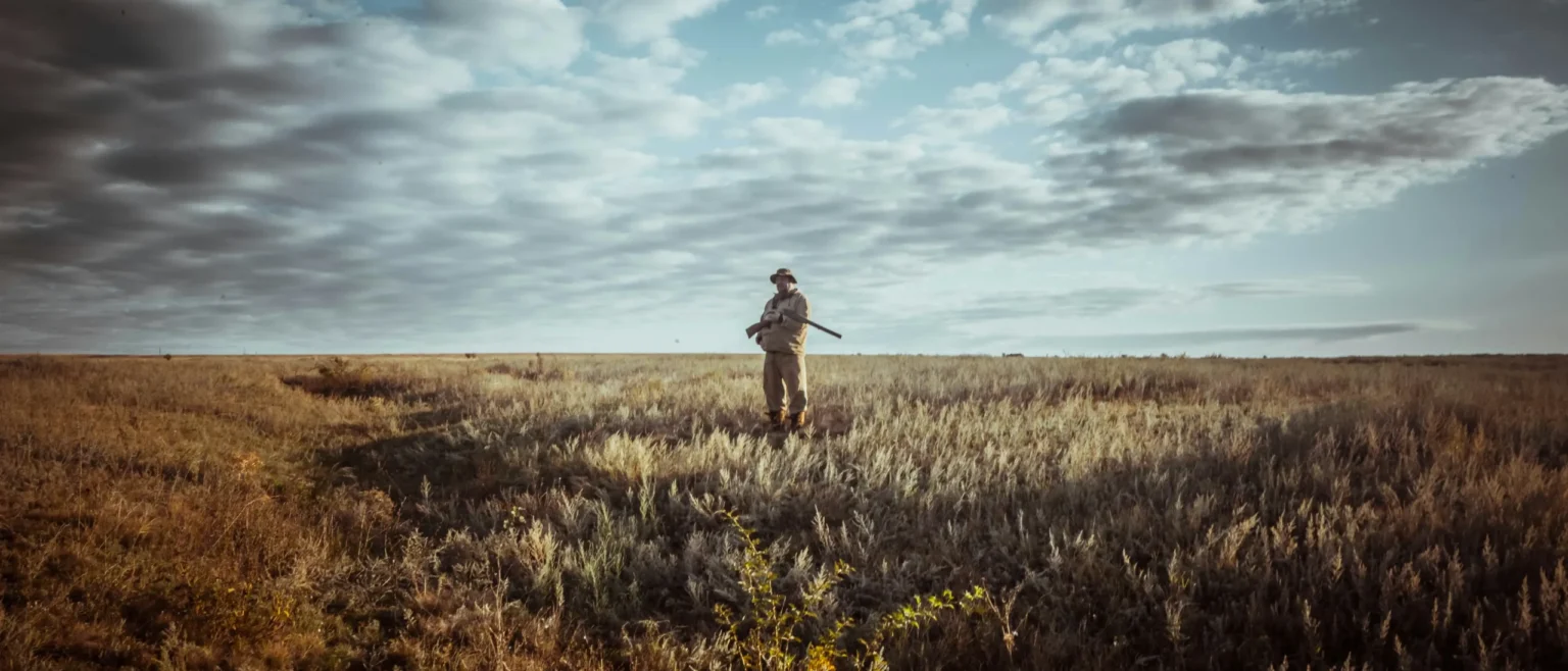 Hunter standing in open grassland holding a rifle during regulated wildlife management and conservation hunting.