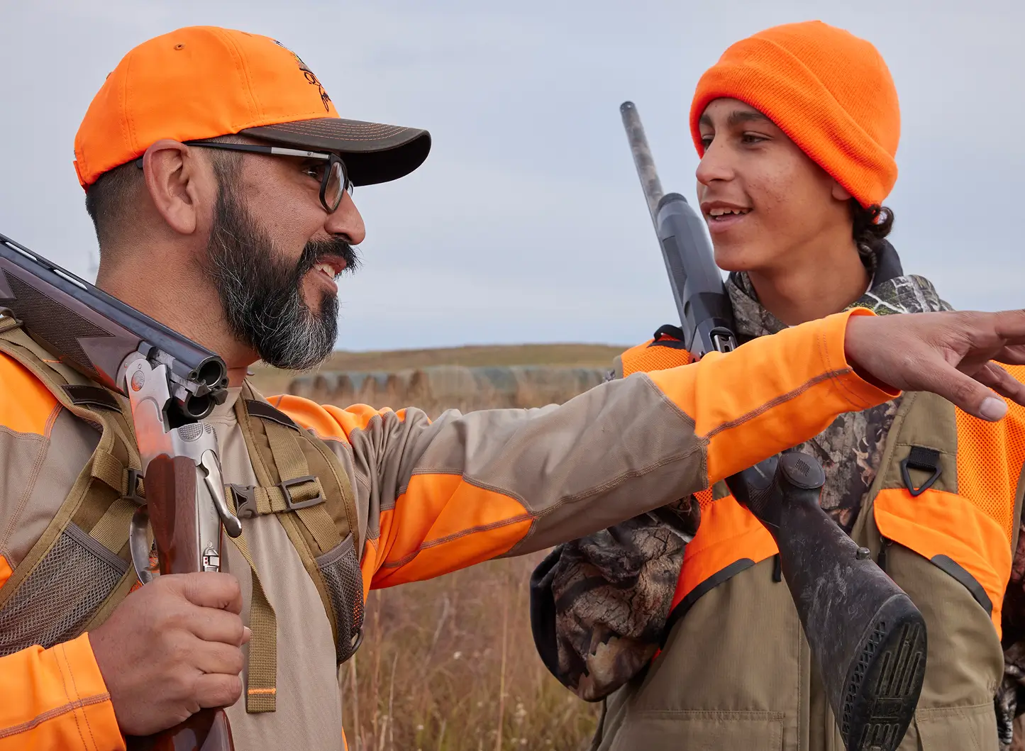 Father and son wearing blaze orange hunting gear and carrying shotguns while preparing for an upland bird hunting trip.