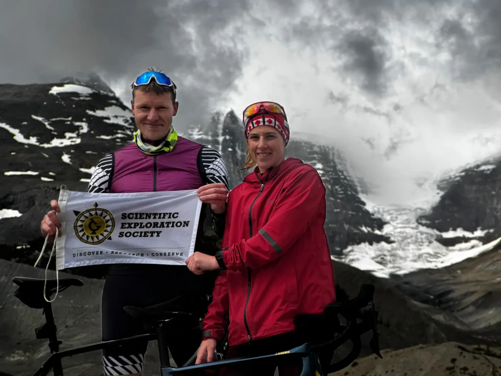 Timm and Leanna holding banner in front of snow-capped mountains and fog